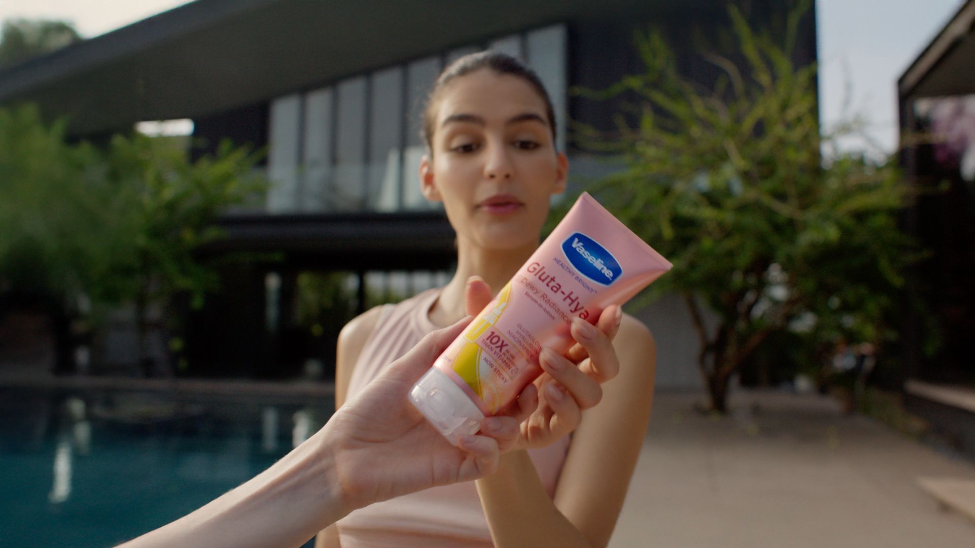 Seorang wanita memegang tabung lotion Vaseline Gluta-Hya berwarna merah muda di luar ruangan.
