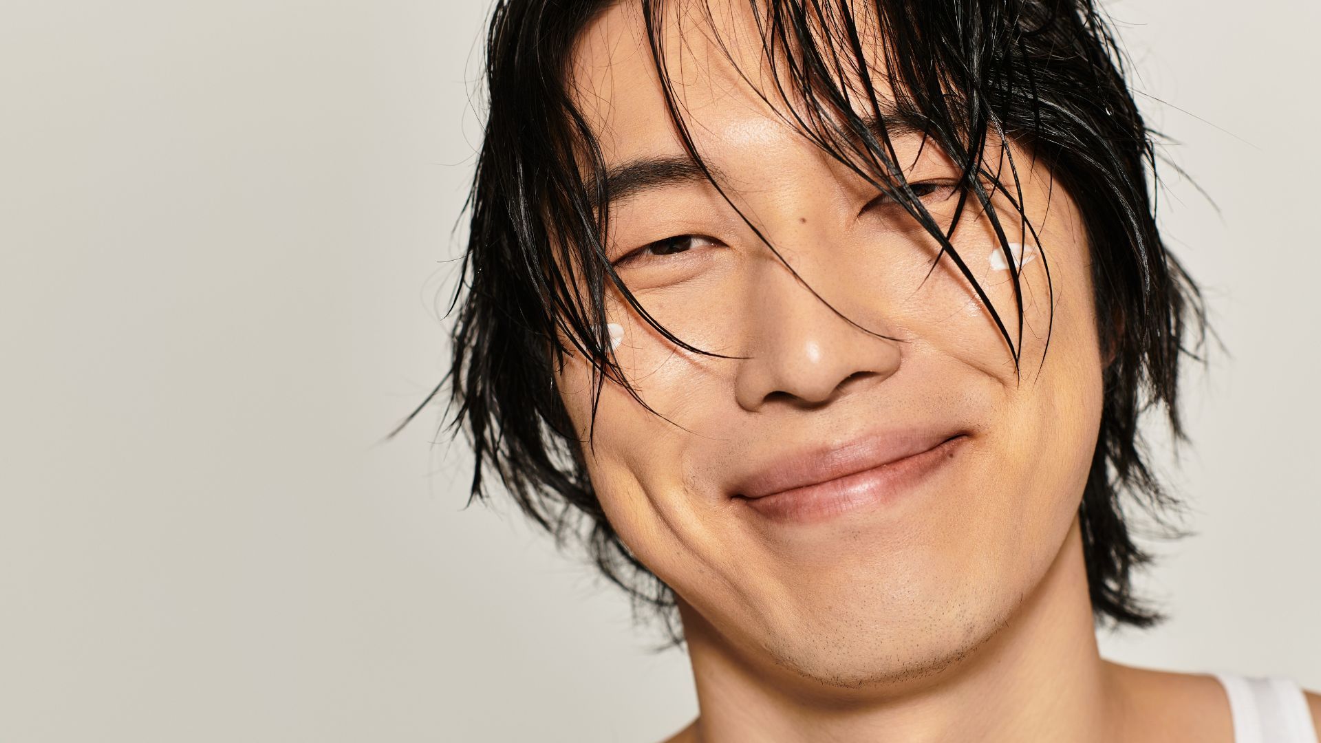 Pria berambut basah tersenyum, dengan bintik-bintik krim di pipi.