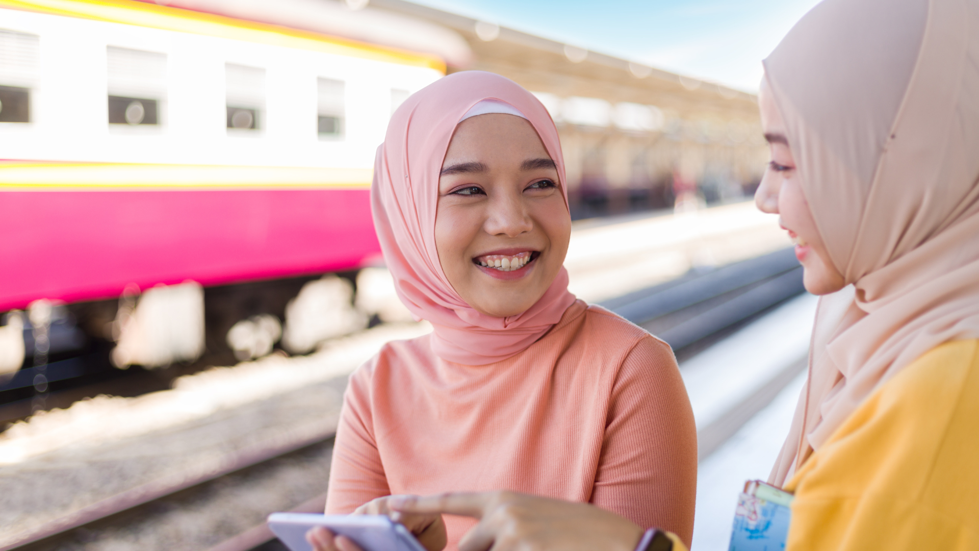 Dua wanita tersenyum di stasiun kereta api.