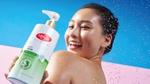 Seorang wanita tersenyum memegang sabun mandi antibakteri Lifebuoy Anti Jerawat -– botol putih dan hijau dengan logo Lifebuoy merah.