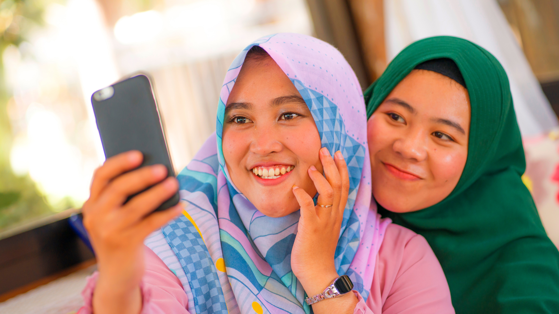 Dua wanita berhijab tersenyum sambil berfoto selfie.