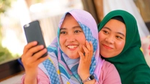 Dua wanita berhijab tersenyum sambil berfoto selfie.
