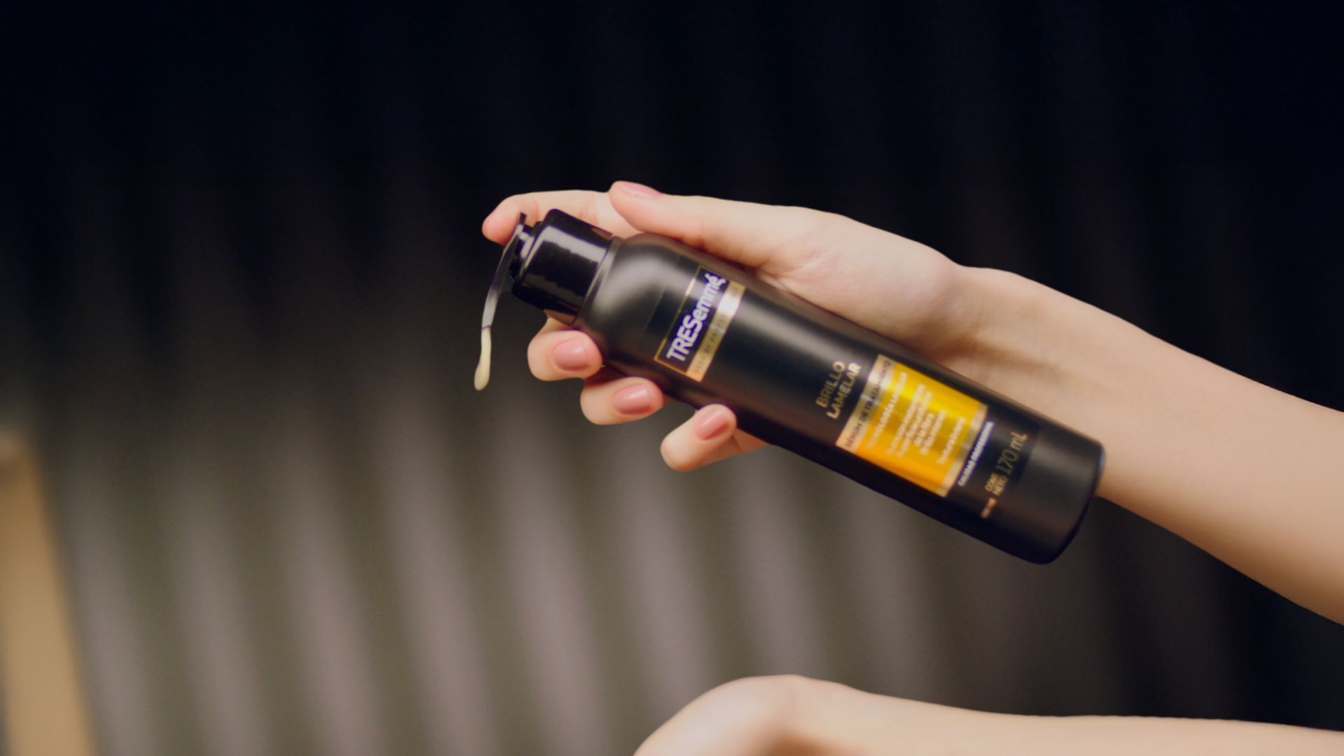 Tangan memegang botol TRESemmé, mengeluarkan produk.